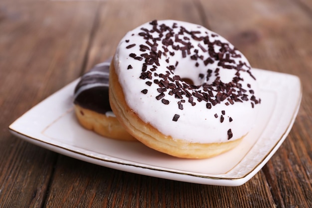 Donuts deliciosos com cobertura em prato em fundo de madeira