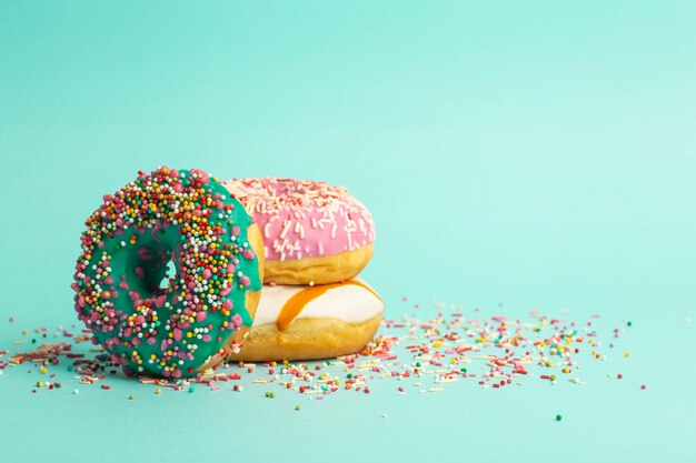 Donuts (donas) de diferentes colores sobre un fondo verde con chispitas de azúcar festivas multicolores. Vacaciones y dulces, hornear para niños, concepto de azúcar