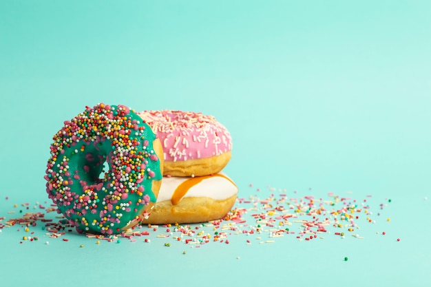 Donuts (donuts) de cores diferentes, sobre um fundo verde com granulado de açúcar festivo multi-coloridas. Férias e doces, assar para crianças, conceito de açúcar