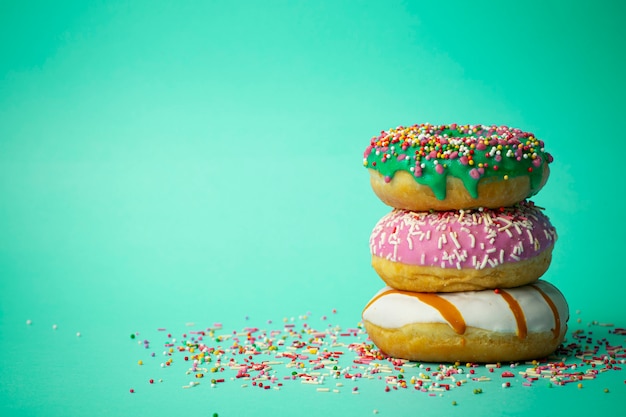 Donuts (Donuts) in verschiedenen Farben auf grünem Hintergrund mit mehrfarbigen festlichen Zuckerstreuseln. Urlaub und Süßigkeiten, Backen für Kinder, Zuckerkonzept