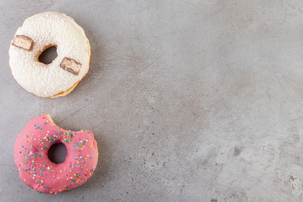 Donuts dulces enteros y mordidos colocados sobre una mesa de piedra.