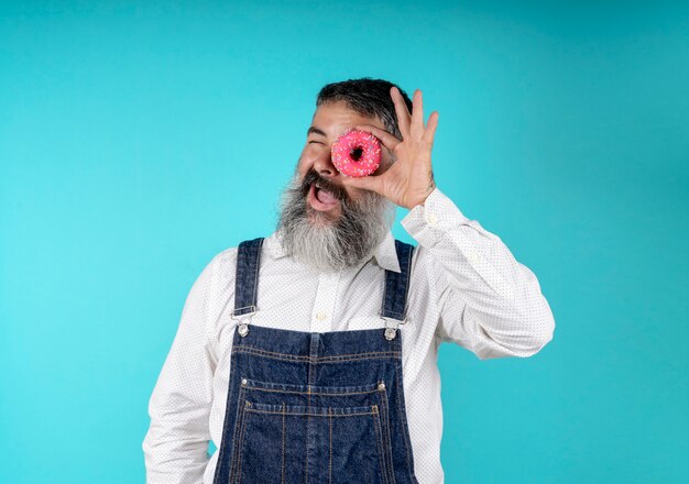 Donuts Essen Backwaren. Süßigkeiten und Kuchen. Junk Food. Bärtiger Hippie mit blauem Brustschild mit süßen Schaumgummiringen um ein Auge auf einem hellblauen