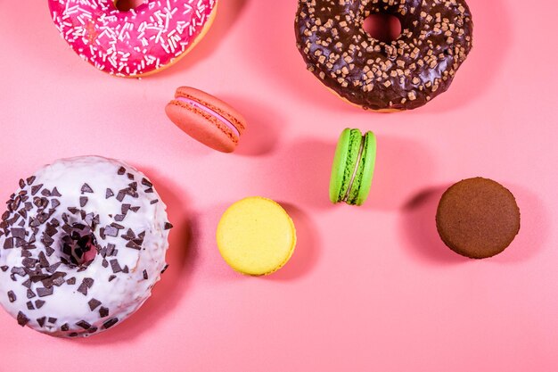 Donuts frescos com cobertura e macaroons franceses isolados em um fundo rosa