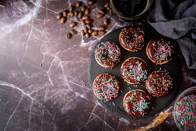 Donuts frescos con glaseado de chocolate y salpicaduras coloridas sobre un fondo oscuro