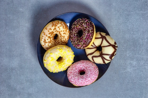 Donuts glaseados dulces coloridos con chispitas de colores sobre placa azul, vista superior