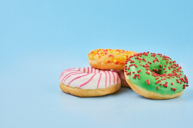 Donuts glasiert mit Streuseln auf pastellblauem Hintergrund. Süße Donuts auf blauem Papier. Nahansicht.