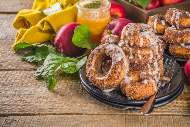 Donuts horneados con azúcar, glaseado de canela y llovizna de cobertura de azúcar blanco, sobre fondo de madera con manzanas frescas