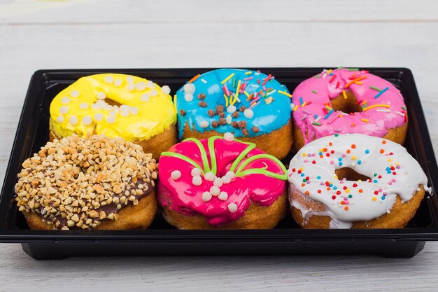 Donuts mit Glasur in einer Schachtel auf weißem Holzhintergrund