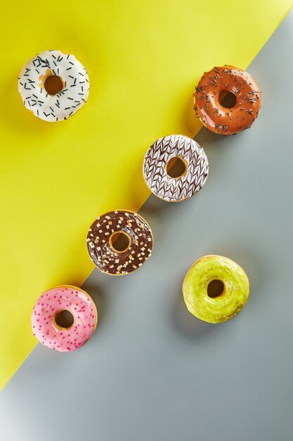 Donuts multicolores con glaseado y chispas sobre fondo amarillo-gris. Endecha plana