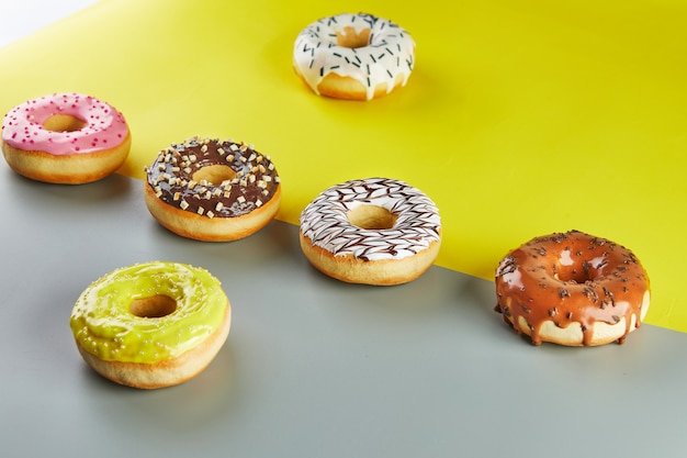 Donuts multicolores con glaseado y chispitas sobre un fondo amarillo-gris