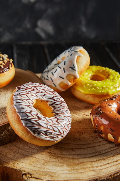 Donuts multicolores con glaseado y rocía en posavasos de madera sobre un fondo negro.