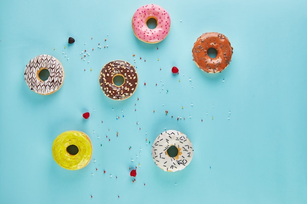 Donuts multicolores con glaseado y rocía sobre fondo azul. Endecha plana