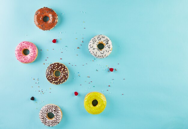 Donuts multicolores con glaseado y rocía sobre fondo azul. Endecha plana