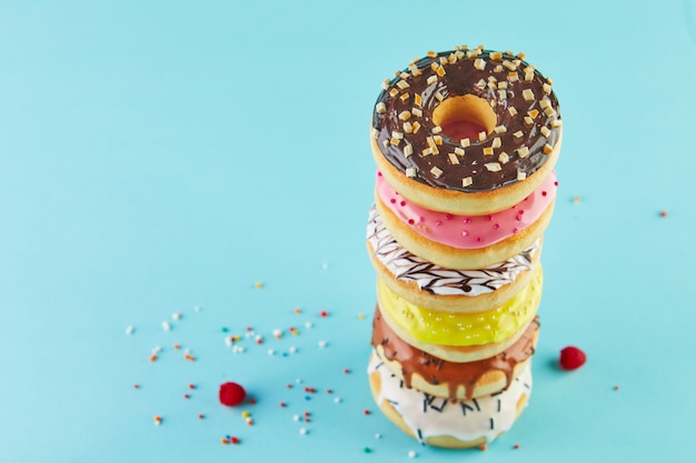 Donuts multicolores con glaseado y rociado apilados en una pila sobre un fondo azul.