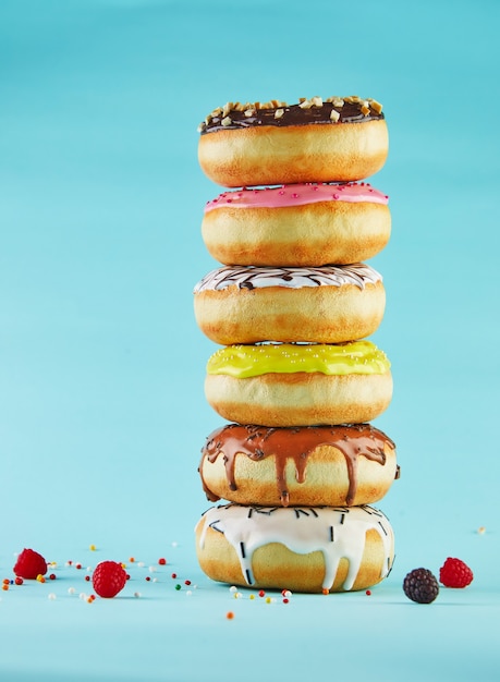 Donuts multicolores con glaseado y rociado apilados en una pila sobre un fondo azul.