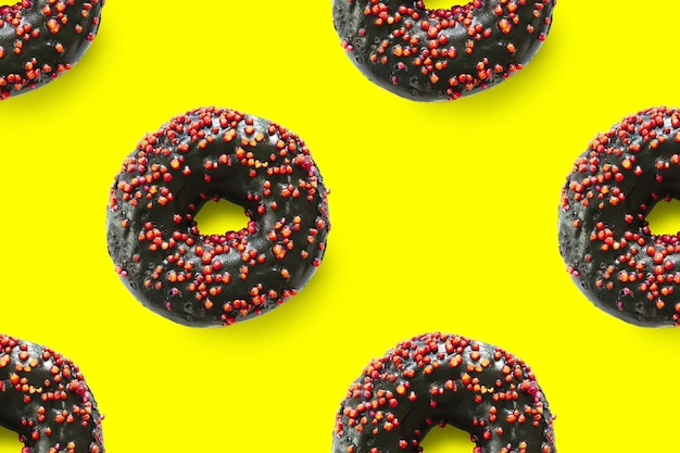 Donuts negros con esmalte rojo sobre fondo amarillo vista superior de patrones sin fisuras. Postre de comida completamente plana laical de deliciosos bocadillos dulces donuts de chocolate