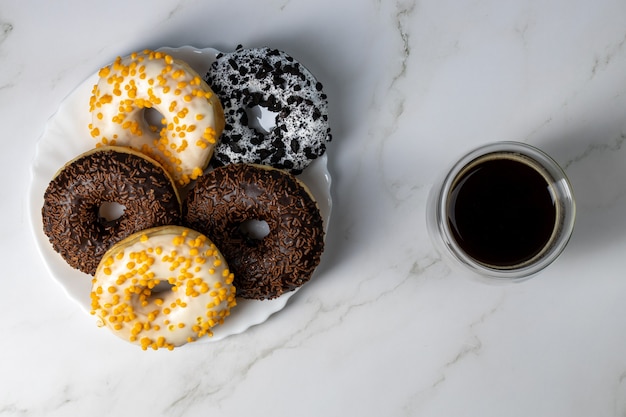 Foto donuts en un plato blanco sobre una mesa de mármol y café