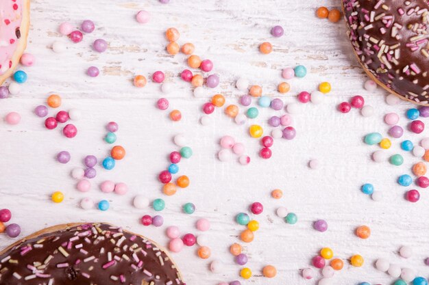 Foto donuts en un plato negro y caramelos sobre fondo blanco de madera. deliciosa comida chatarra