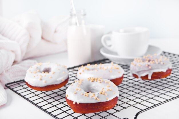 Donuts en la rejilla para hornear crema de chocolate blanco glaseado o glaseado. Botella con leche y taza de café en el fondo