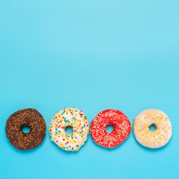 Donuts sabrosos de diferentes tipos en un espacio azul. Concepto de dulces, panadería, repostería. Cuadrado. Vista plana endecha, superior.