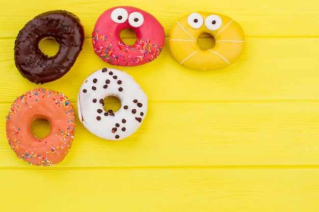 Donuts sobre fondo amarillo con espacio de copia. Borde lateral de rosquillas variadas con glaseado y chispas de colores pastel.