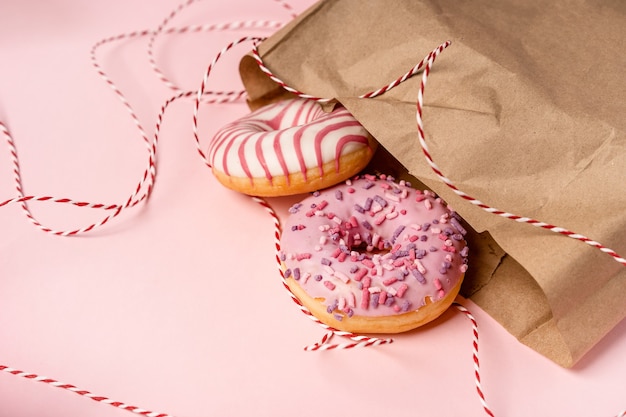 Donuts sobresalen de una bolsa de papel ecológica sobre un fondo rosa