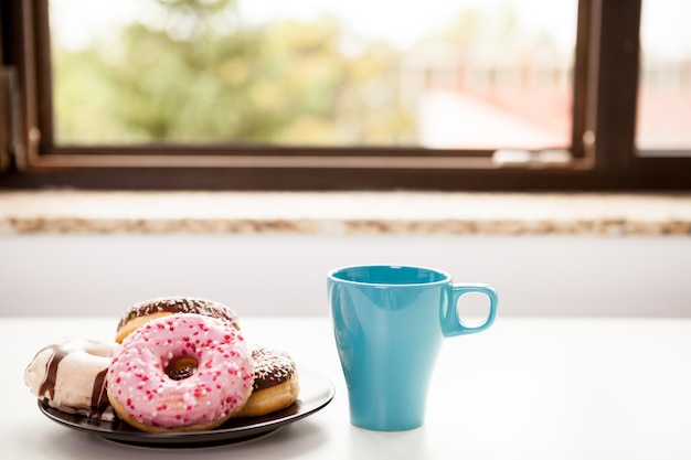 Donuts und eine Tasse Kaffee neben der Fensterbank. Leckeres Junkfood