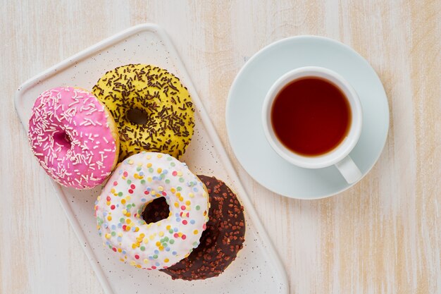 Donuts und Tee. Helle, bunte Junk-Food. Heller beige hölzerner Hintergrund. Ansicht von oben.