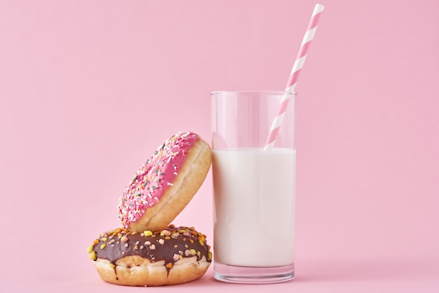 Donuts con vaso de leche sobre fondo rosa