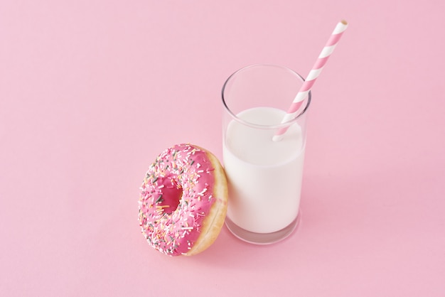 Donuts con vaso de leche sobre fondo rosa