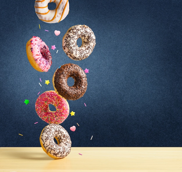 Donuts voladores. Mezcla de rosquillas dulces multicolores con sprinkel cayendo sobre la mesa sobre fondo de textura azul oscuro.