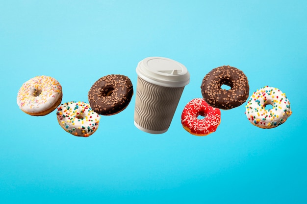 Donuts volando en el aire y la taza de papel de café en un azul. Panadería, concepto de cocción.