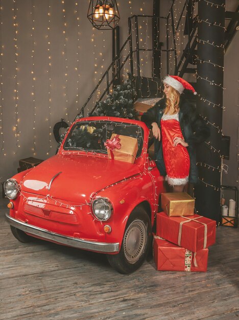 Donzela de neve bonita jovem em decorações festivas e um carro vermelho com presentes e árvore de natal