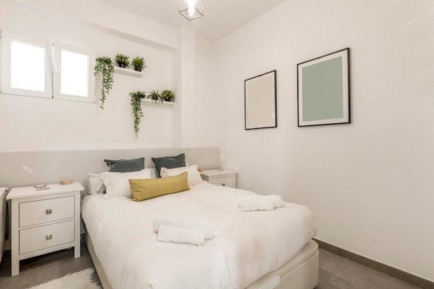 Doppelbett mit blaugoldenen und weißen Kissen und Kissen, weißen gerollten Handtüchern und weißen Regalen mit dekorativen Pflanzen