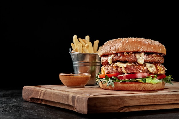 Doppelburger mit Pommes und Sauce auf Holzbrett