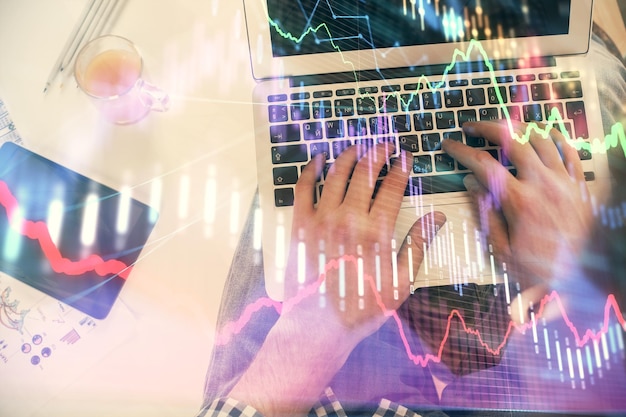 Doppelte Exposition der Händen eines Mannes, der über eine Laptop-Tastatur und ein Forex-Chart-Hologramm zeichnet Top-View Konzept der Finanzmärkte