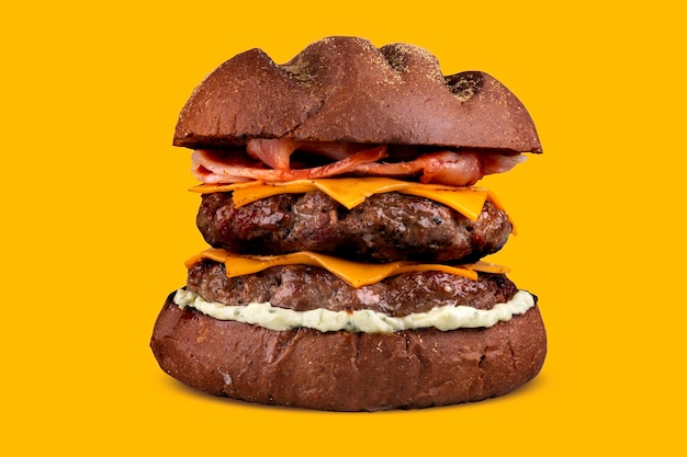 Doppelter Hamburger mit Cheddar und Speck und dunklem australischem Brot isoliert auf gelbem Hintergrund