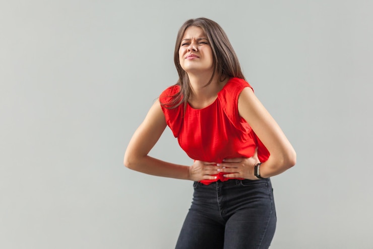 Foto dor de barriga de estômago retrato de jovem morena triste doente de camisa vermelha em pé e segurando seu doloroso problema de barriga tiro de estúdio interior isolado em fundo cinza