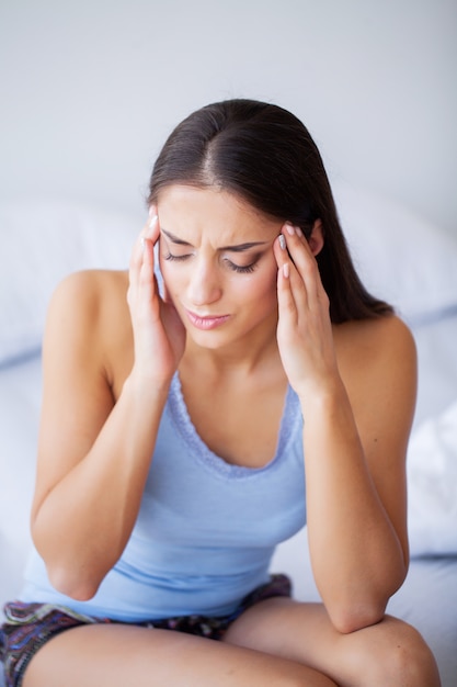 Foto dor de cabeça. a jovem mulher atrativa acorda em sua cama que olha infeliz e que sente doente.
