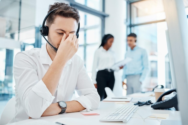 Dor de cabeça de call center e esgotamento de um homem no atendimento ao cliente ou suporte com fadiga ocular no escritório Homem de negócios ou funcionário em telemarketing que sofre de dor de cabeça no local de trabalho da empresa