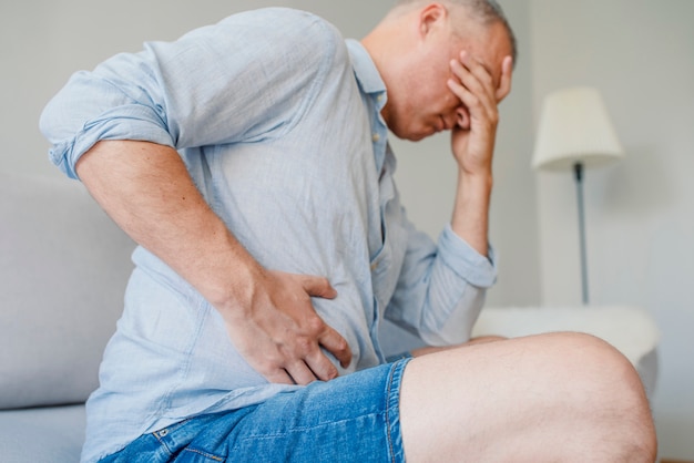 Foto dor de estômago terrível. jovem bonito frustrado abraçando sua barriga e mantendo os olhos clo