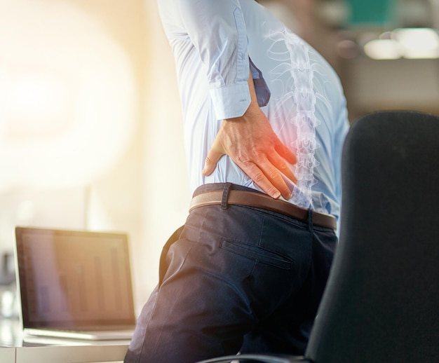 Dor nas costas do empresário e raio x da coluna de sentar e trabalhar com o laptop na cadeira da mesa no escritório Funcionário masculino sofrendo lesão na coluna ou disco deslizante com inflamação da dor ou articulação dolorosa