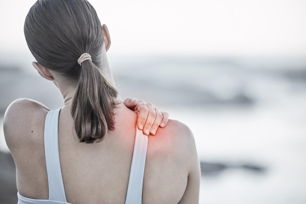 Dor nas costas e lesão com uma mulher de esportes segurando seu ombro durante um treino de exercício na praia Saúde e bem-estar da aptidão com um CGI digital ou sobreposição em uma mão feminina ao ar livre na natureza