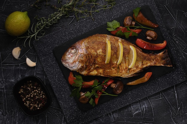 Dorada de peixe grelhado com ingredientes assados e limão na bandeja escura vista superior espaço para cópia grátis