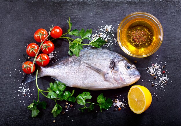 Dorado de peixe fresco com ingredientes para cozinhar em vista superior escura