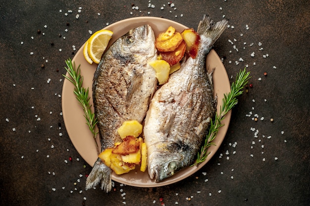 dorado dorado a la parrilla y papas fritas en un plato con especias y limón sobre un fondo de piedra