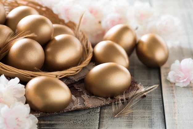 Dorado de huevos de pascua en nido con flor rosa y pluma.