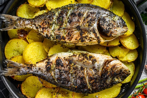 Dorado a la plancha pescado con patatas en una sartén. Fondo gris vista superior