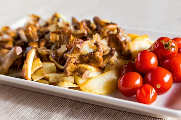 Dorffrühstück - gebratene Kartoffeln und Pilze mit Tomaten auf weißer Platte