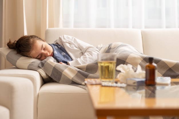 Dormir joven enferma acostada en un sofá con fiebre alta y resfriado.